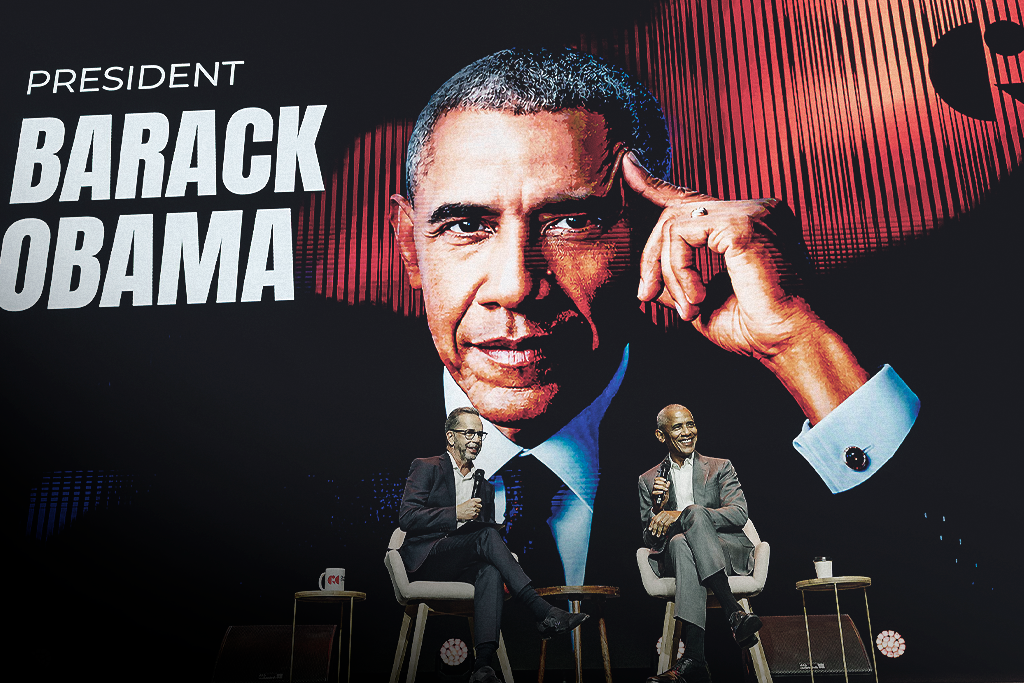 Barack Obama em conversa no palco do Game Changers Forum, com um ecrã gigante a apresentar a identidade visual do evento.